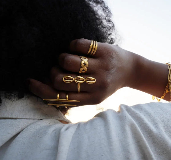 Hand wearing multiple gold african rings from the jewelry brand Doore Dasi with a blurred background